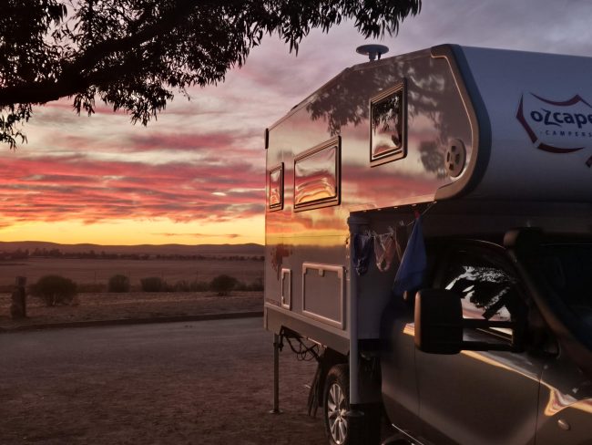 Ozcape camper at sunset in the bush with the stunning colours of the skies refelected in the shiny walls of the Slide-On