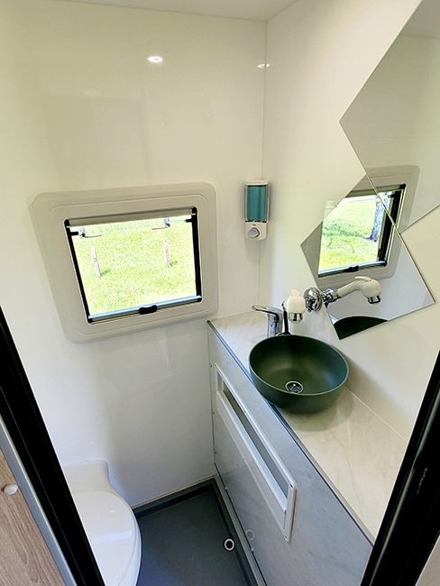 Bathroom of an Ozcape Slide-On with shower, toilet, vanity and window. Complete with shelf, mirror and soap dispenser.